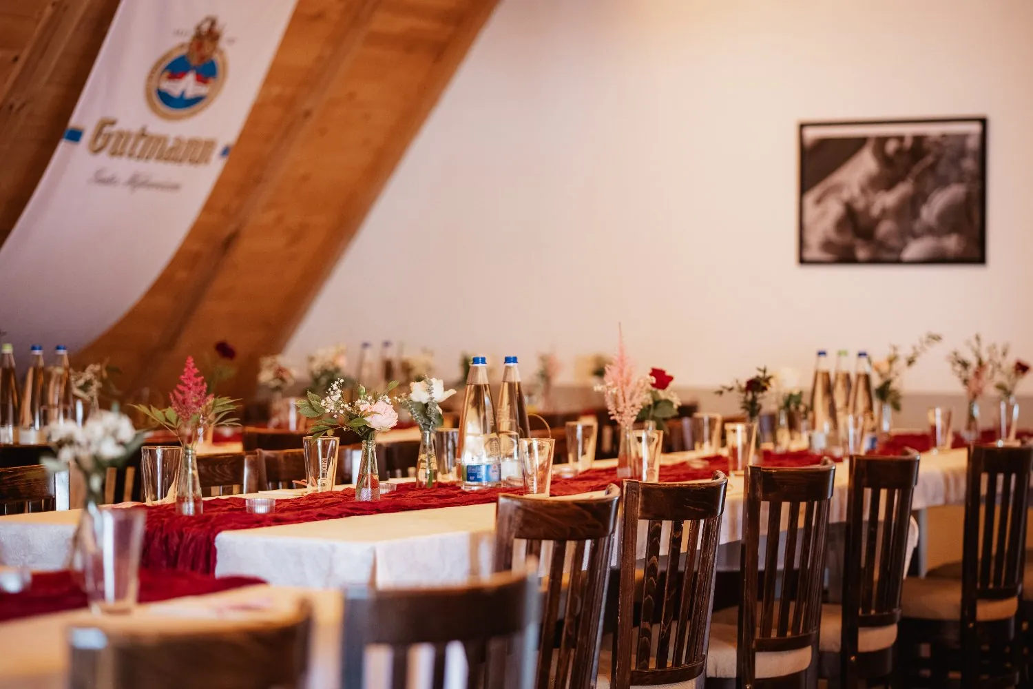 Eingedeckte Festtafel mit roten Läufern und Blumen im Stodl